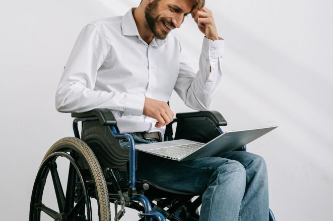 Man in wheelchair working on a laptop indoors, showcasing accessibility and technology.